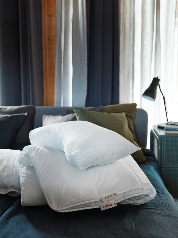 A SMÅSPORRE duvet and a SKOGSLÖK ergonomic pillow are piled-up together on a blue bed in a blue-toned bedroom.