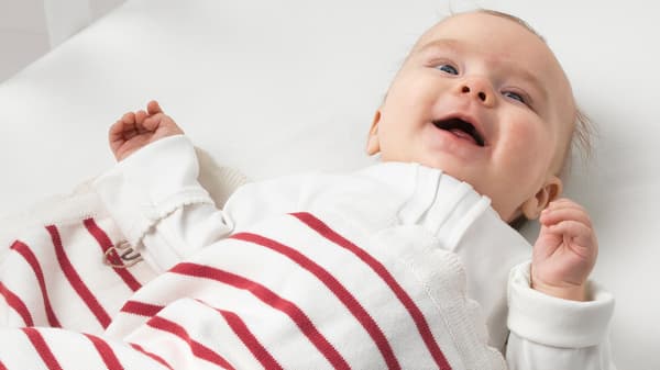 A smiling baby with a white and red striped RÖDHAKE blanket made from responsibly grown cotton.