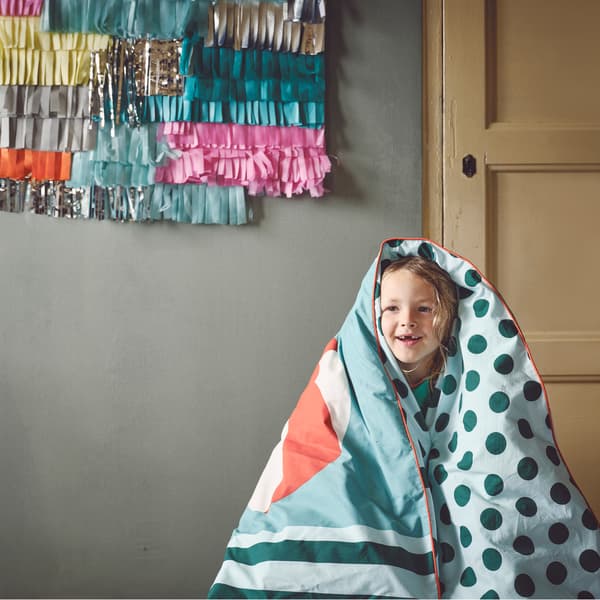 A smiling child is wrapped in a cozy KÄPPHÄST quilt cover with light and dark green polka dots and stripes.