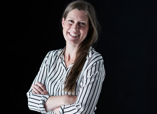A smiling Elin Stierna, IKEA interior designer, against a black background, dressed in a black and white striped shirt