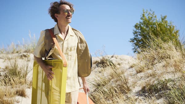 A smiling man walking through sand with a cooler and folded lawn chair