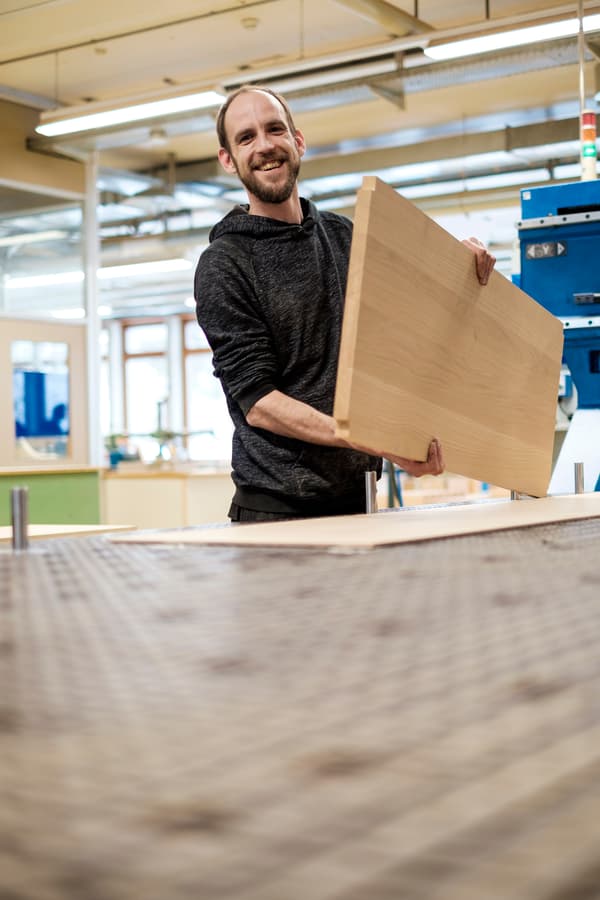 A smiling VEBO co-worker holds a cut wooden board in his hand. 