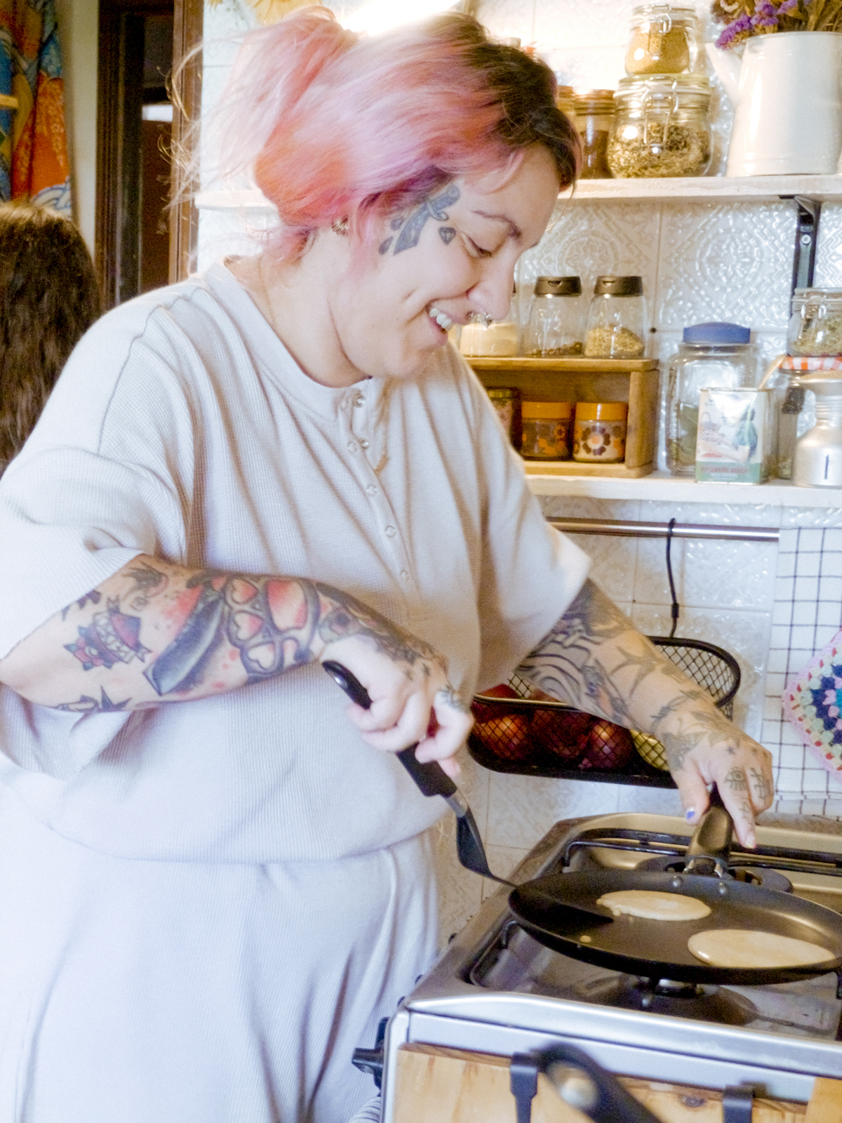 A smiling woman is making pancakes in a HEMLAGAD pancake pan on the stove.