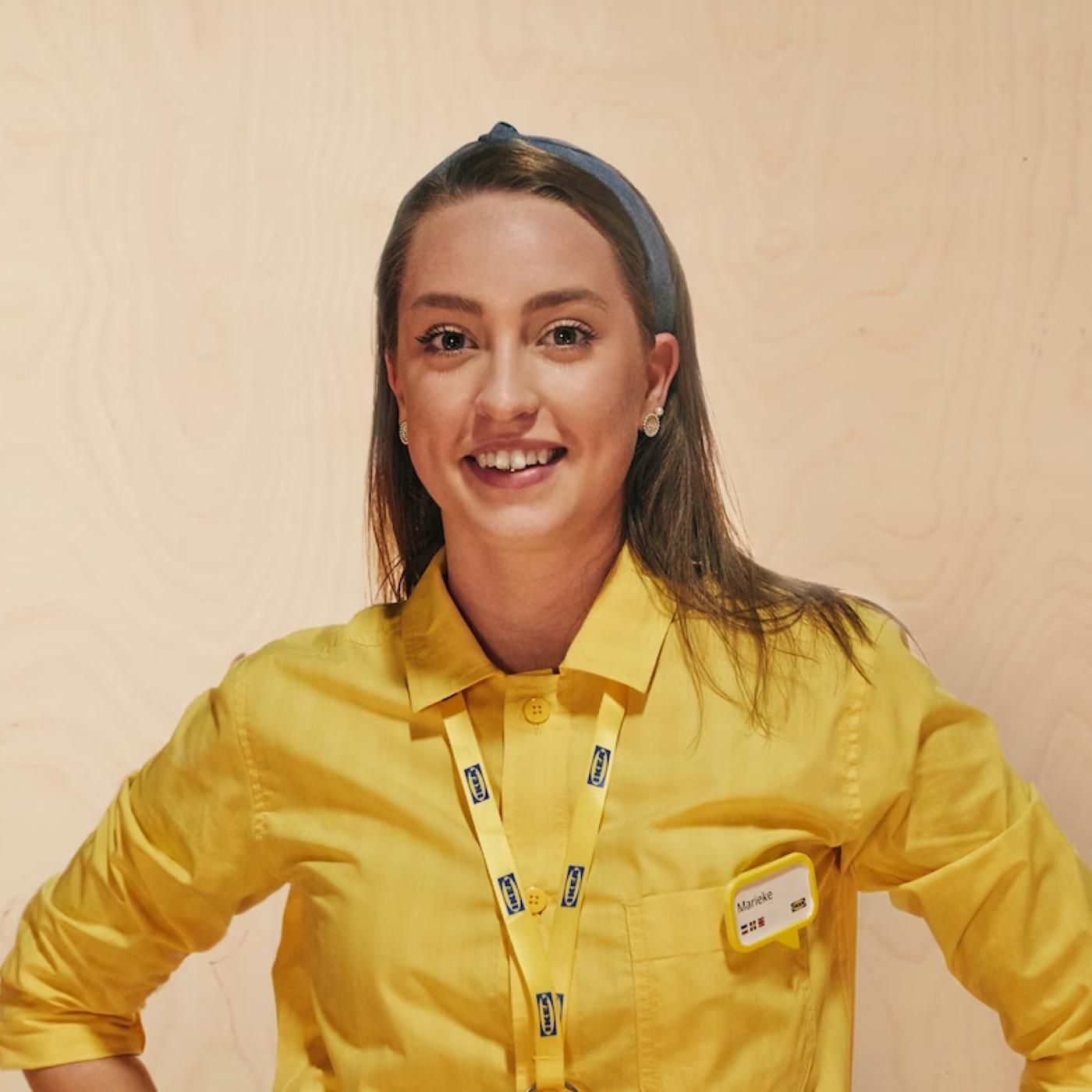 A smiling woman with brown hair smiles while wearing a yellow ikea