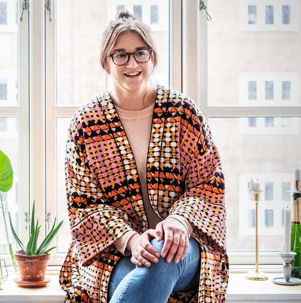 A smiling young woman wearing a colorful kaftan sitting in a window frame