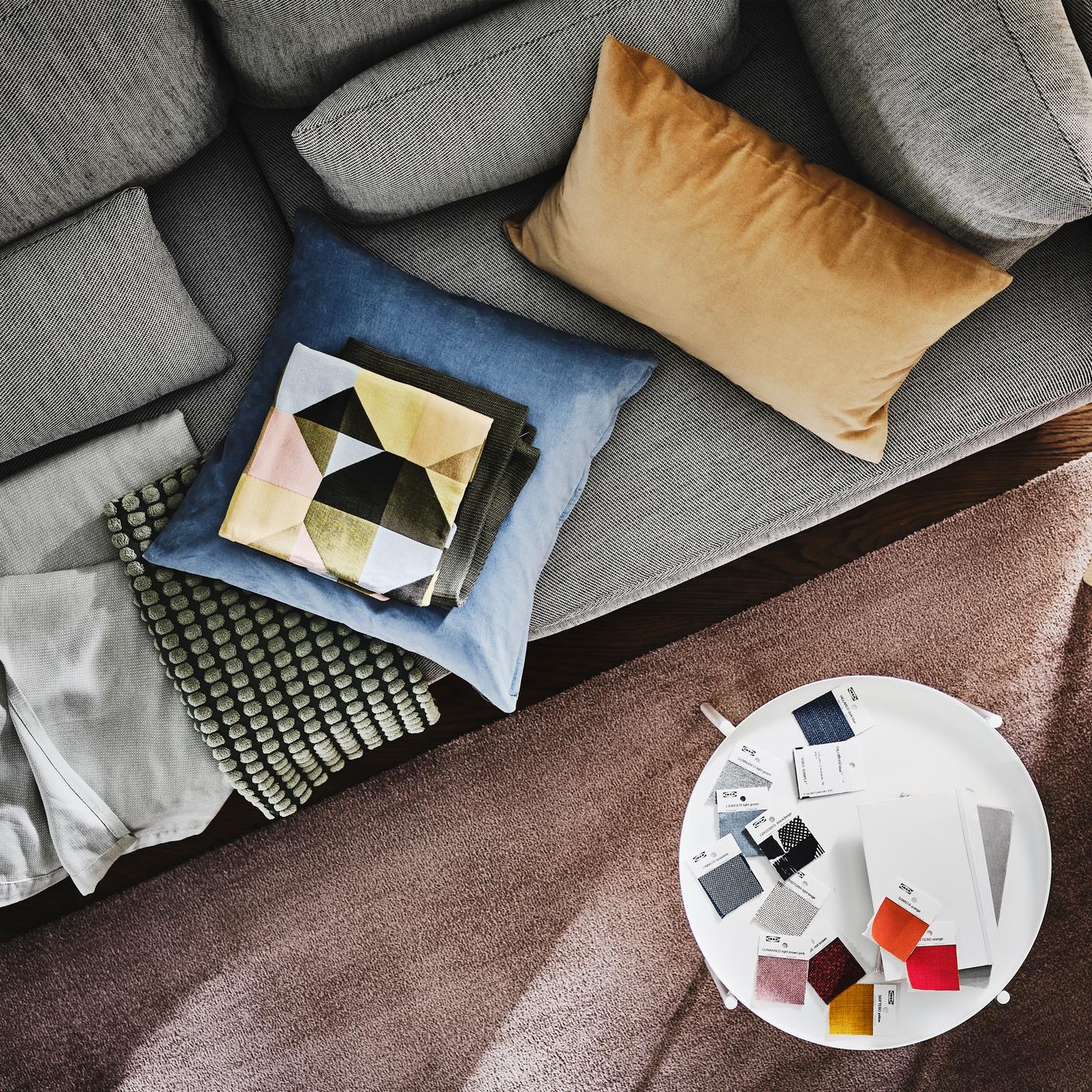 A SÖDERHAMN 3-seat sofa with cushions and a light pink throw on it is by a side table with colour swatches on it.