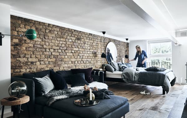 A sofa and bed against an exposed brick wall.