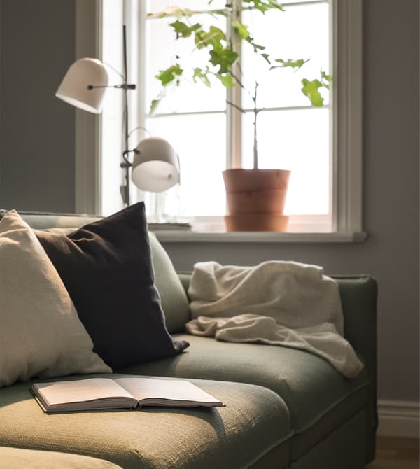 A sofa with cushions and a blanket sit in front of a window.
