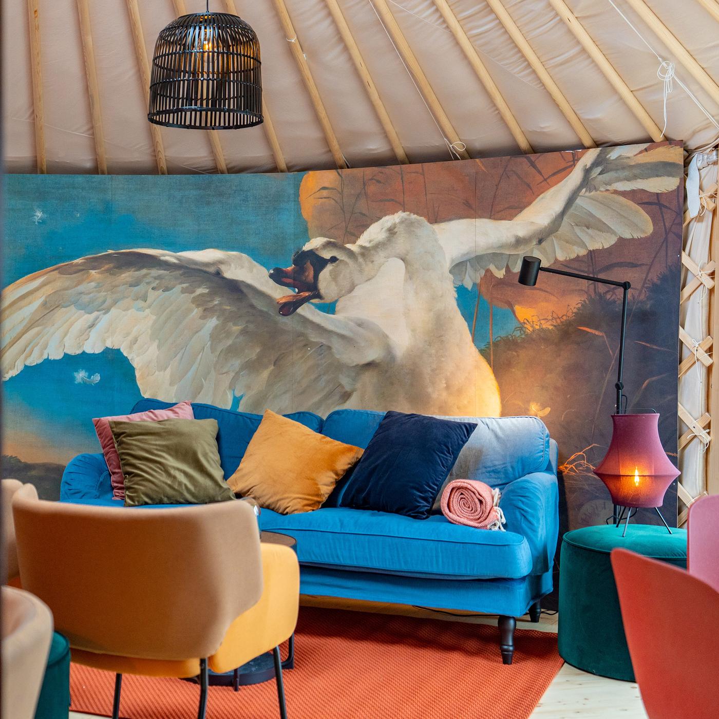 A sofa with various pillows in a yurt in front of a wall with a floor-to-ceiling picture of a swan