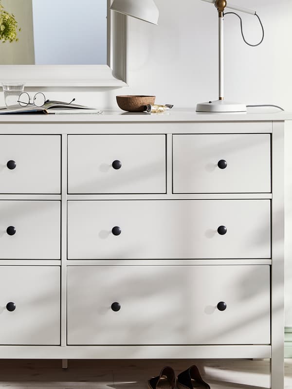 A softly lit white HEMNES eight-drawer chest of drawers with a lamp, a bowl, and a pair of glasses on top.
