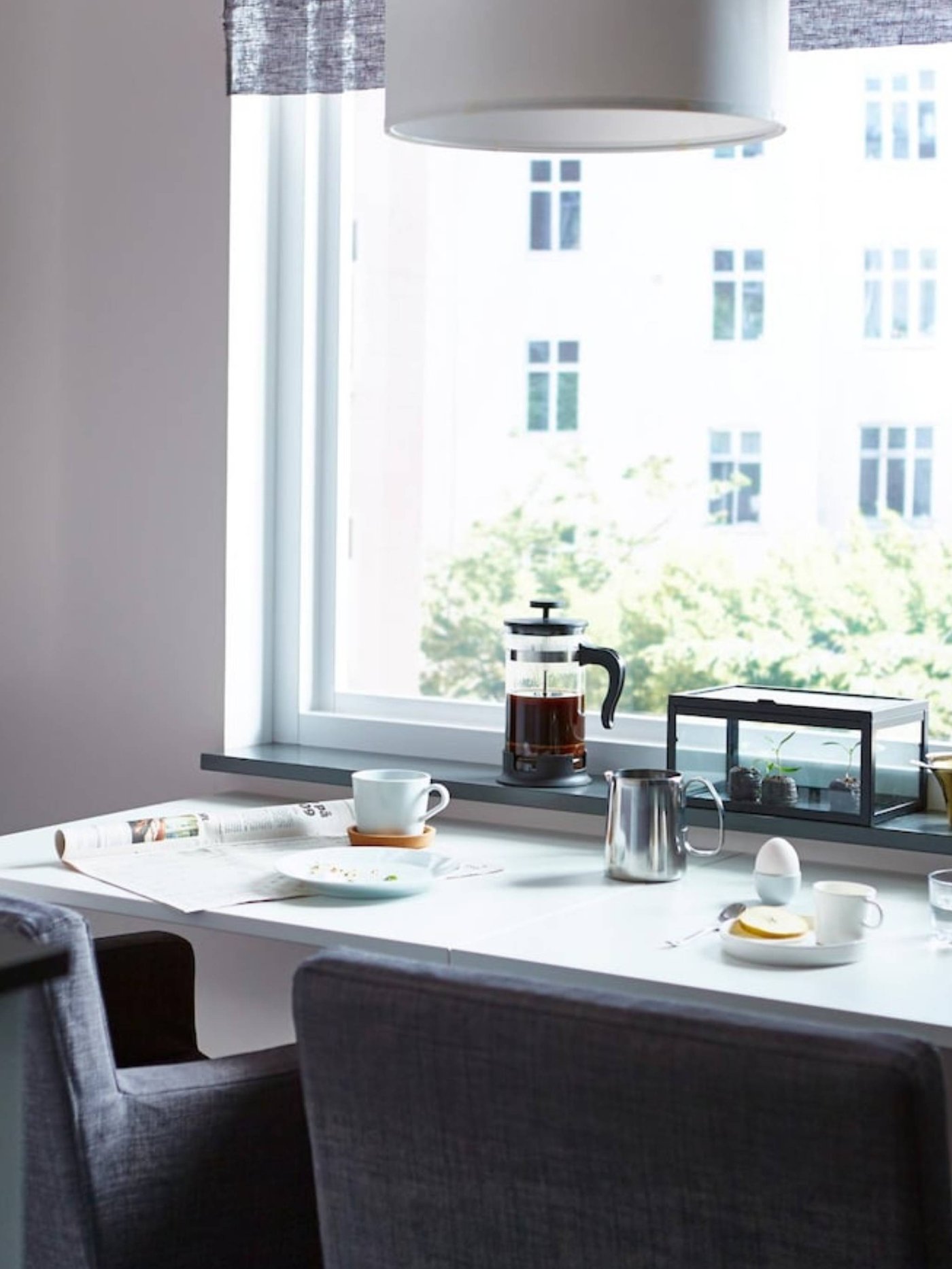 A space-saving dining table, prepared with breakfast, with two dining chairs facing a window.