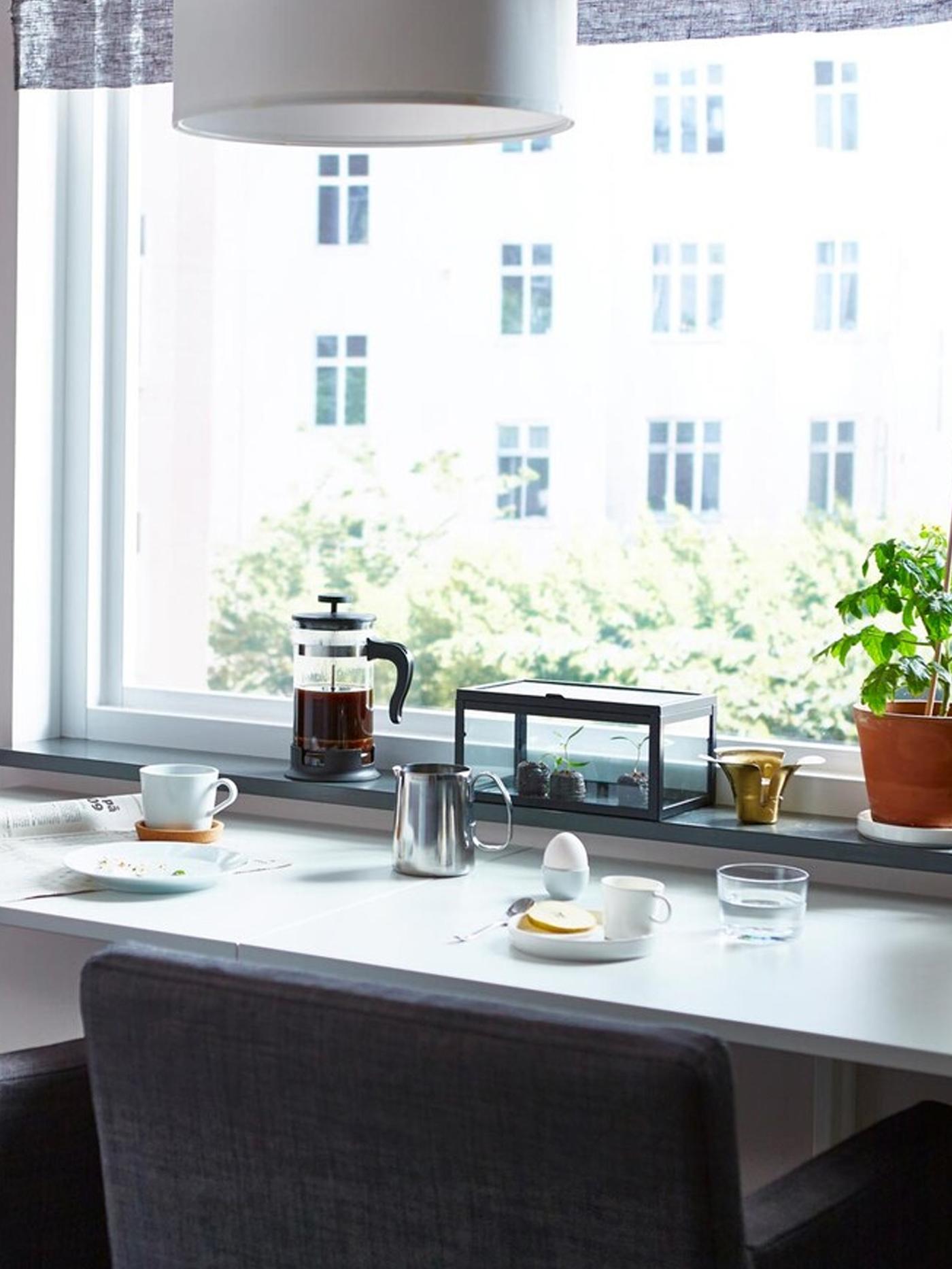 A space-saving dining table, prepared with breakfast, with two dining chairs facing a window.