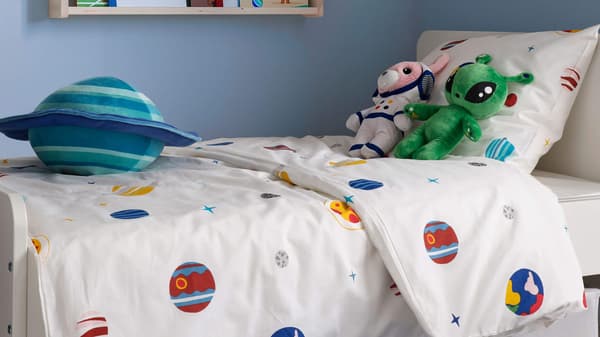 A space themed kid's bedding and various space soft toys sitting on top of the bed
