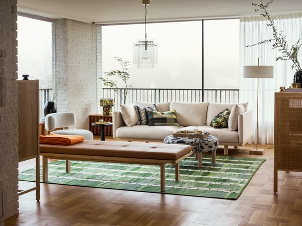 A spacious, light-filled living room featuring a neutral sofa, a wooden coffee table, a woven rug, and a pendant light, blending natural textures.