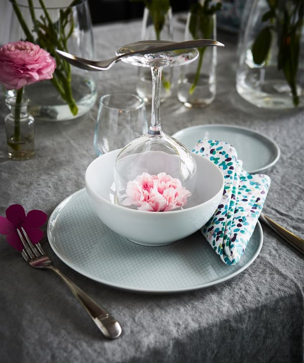 A springtime place setting with a wine glass, a pink flower, and a gray plate.