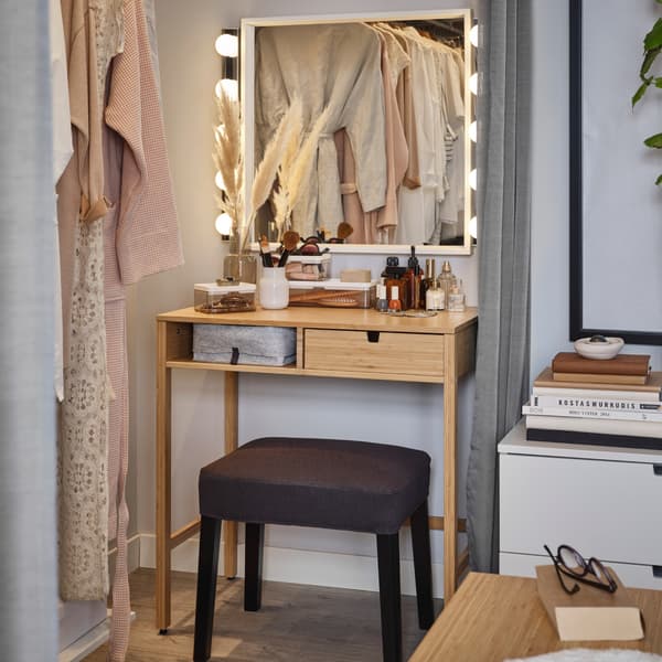 A square mirror, a dressing table in bamboo, two LED wall lamps and a dark grey stool offer a complete beauty station.