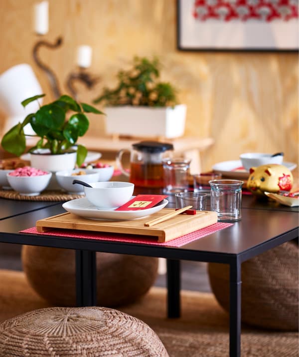 A square RIMFORSA chopping board in bamboo used as an Asian style placemat, on a black table.