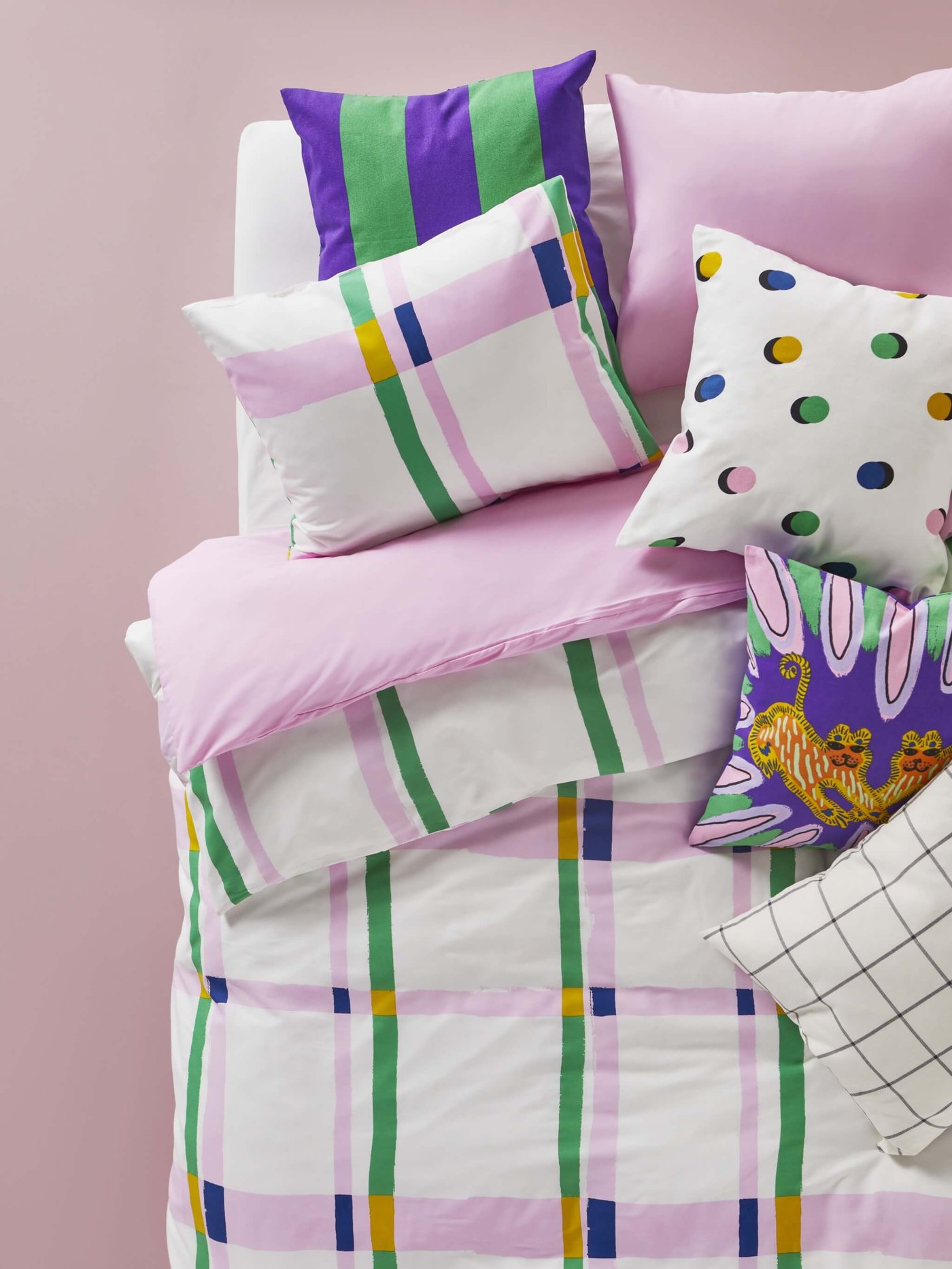 A stack of colorful pillows and bedding against a pink background.