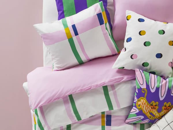 A stack of colorful pillows and bedding against a pink background.