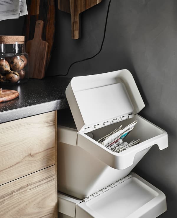 A stack of flip-top waste bins in the empty space under a kitchen worktop at the end of a row of ash effect base cabinets