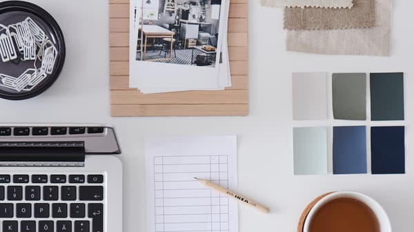A stack of inspirational interior design photos, a checklist, and an IKEA pencil are on top of a light desktop.