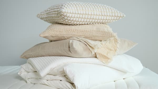 A stack of neutral colored bed textiles on a white mattress.