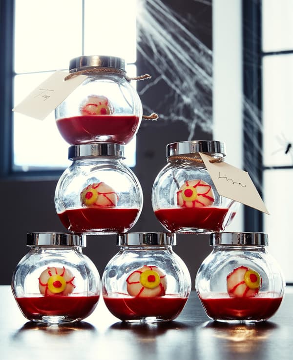 A stack of small glass jars filled with red gelatin and treats that look like eyeballs.