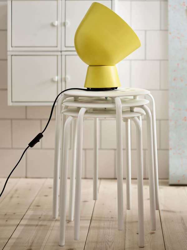 A stack of white stools with a yellow table lamp on top.