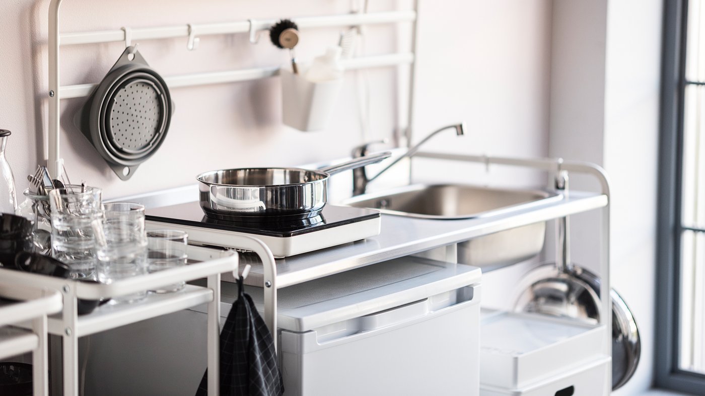A stainless steel frying pan on a TILLREDA portable induction hob on a white SUNNERSTA kitchenette.