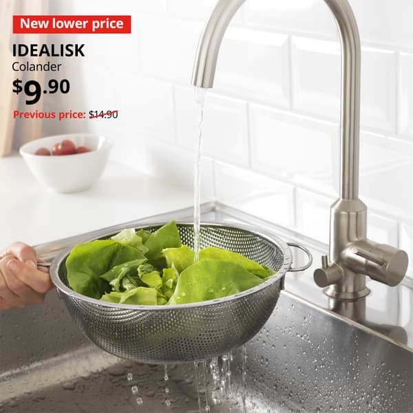 A stainless steel IDEALISK colander with greens being washed under the running tap in a kitchen setting. Image with New lower price tag. Price: $9.90. Usual price with red slash: $14.90.