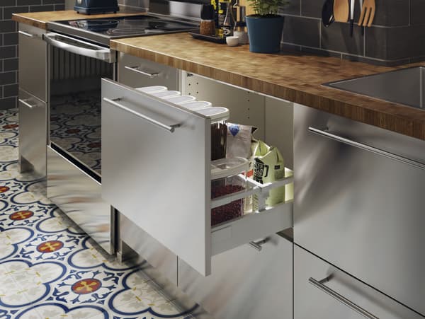 A stainless steel kitchen with a wood worktop in oak/veneer. One drawer is open, and lots of dry goods are stored inside.