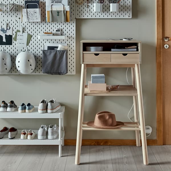 A standing desk in white birch, a white shoe shelf and white wall-mounted pegboards where helmets and more things are stored.