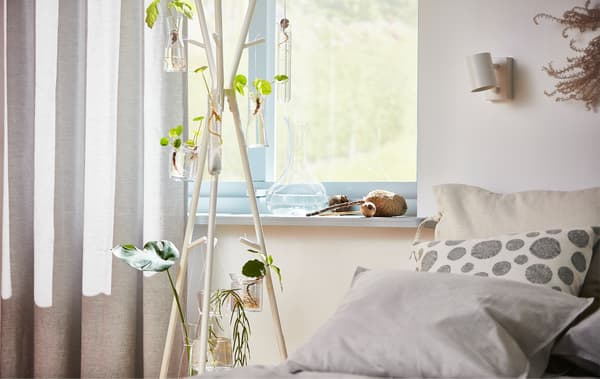 A standing white EKRAR hat and coat hanger in front of a window with bed pillows next to it.
