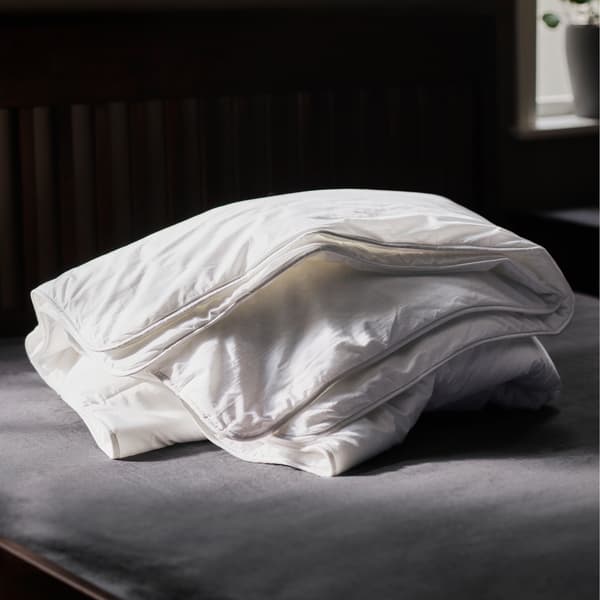 A STJÄRNBRÄCKA warm duvet folded up on a grey mattress in a dark room near a window with a plant on the sill.