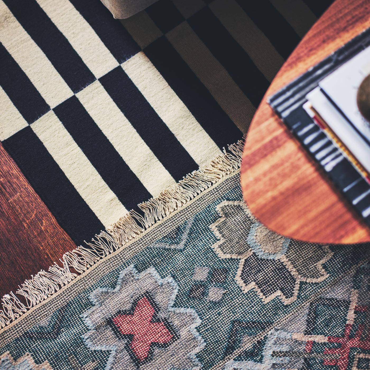 A STOCKHOLM coffee table with walnut veneer placed on a VESTERVIG flatwoven rug and a striped STOCKHOLM flatwoven rug.