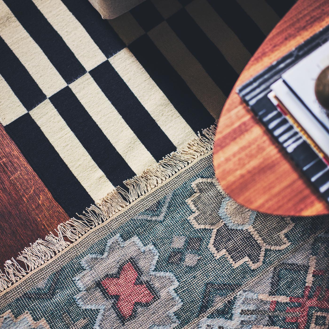 A STOCKHOLM coffee table with walnut veneer placed on a VESTERVIG flatwoven rug and a striped STOCKHOLM flatwoven rug.