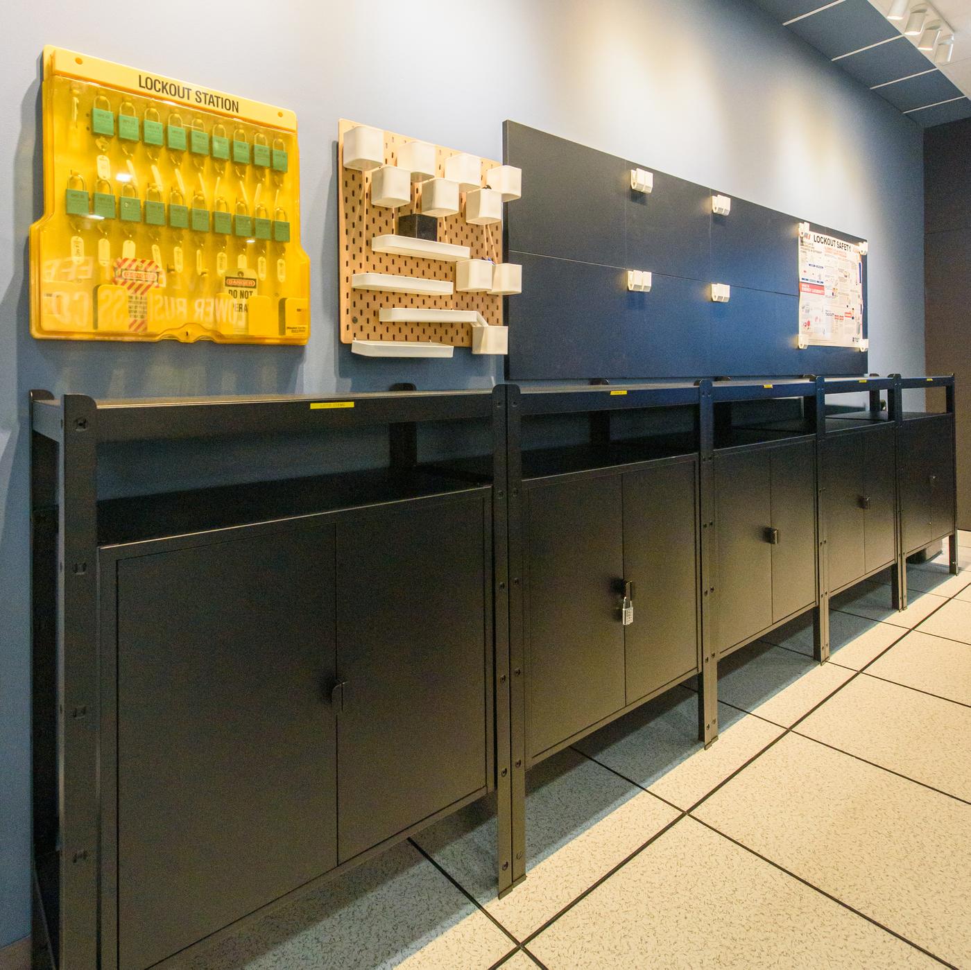 A storage area with black cabinets with pegboards on the wall on top.