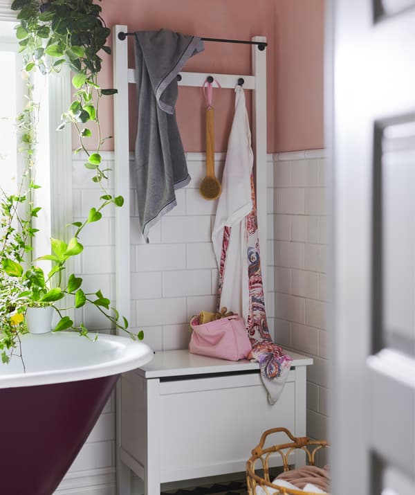 A storage bench with hooks and a rail next to a bath and plants.