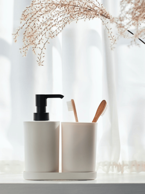 A STORAVAN soap dispenser and a STORAVAN toothbrush holder holding two toothbrushes stand on a white surface.