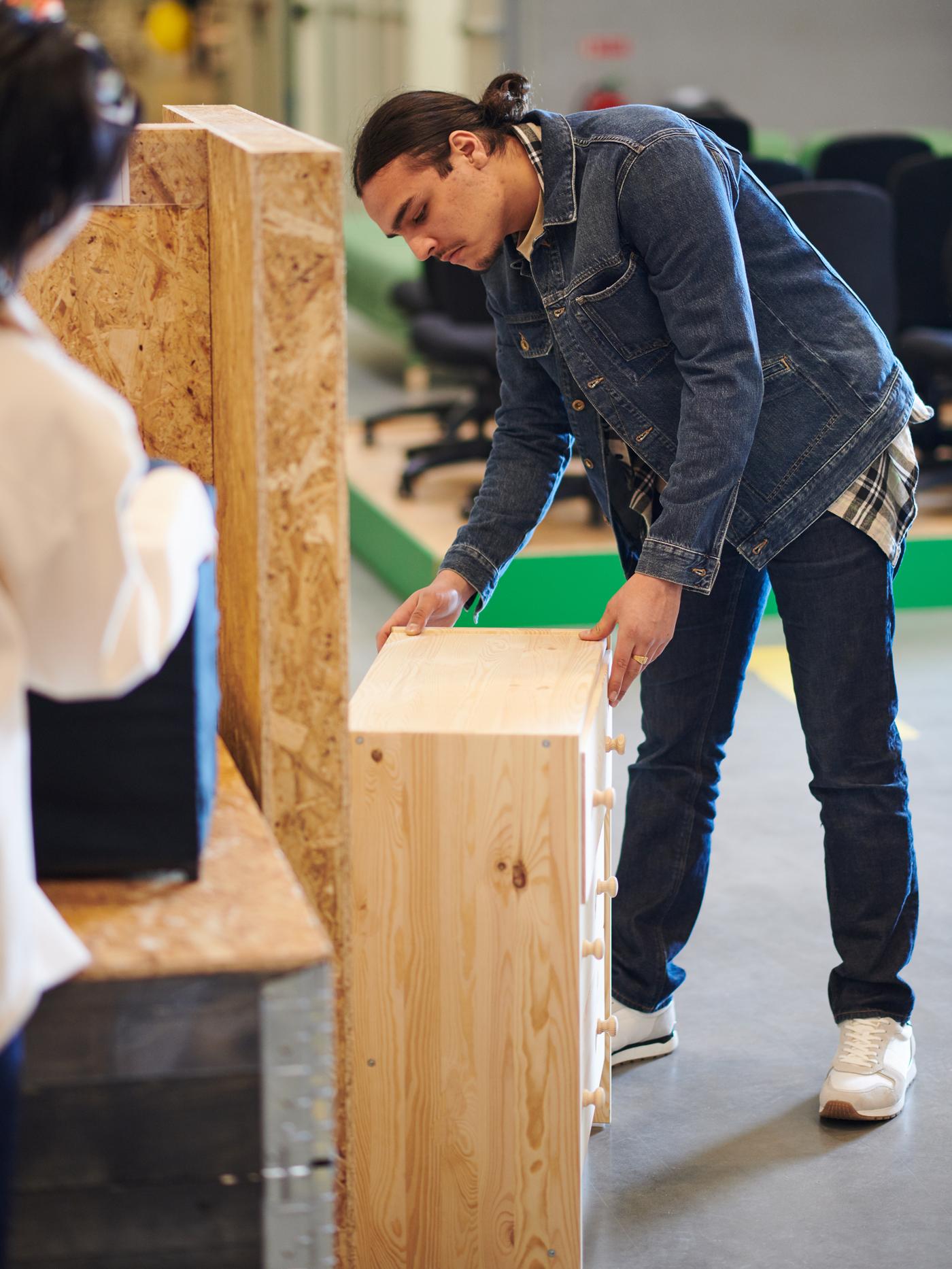 A store interior where a man inspects an untreated, natural-wood chest of drawers.