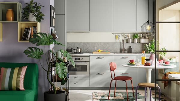 A straight kitchen with light grey HAVSTORP fronts has a white DOCKSTA table, a red-brown ÖSTANÖ chair, and a DOMSTEN stool.