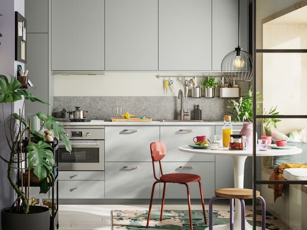 A straight kitchen with light grey HAVSTORP fronts has a white DOCKSTA table, a red-brown ÖSTANÖ chair, and a DOMSTEN stool.