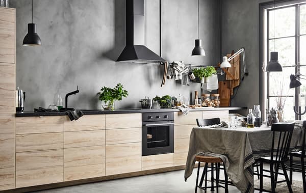 A straight-line kitchen with a row of base cabinets with ash fronts against a grey, concrete looking wall  