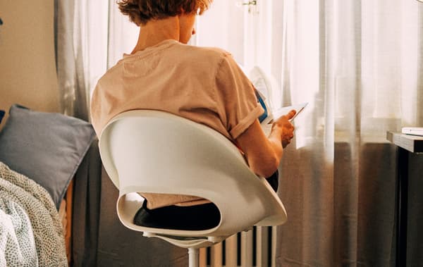 A student sits in a swivel chair facing the window, his feet resting on the radiator in front of him as he studies.