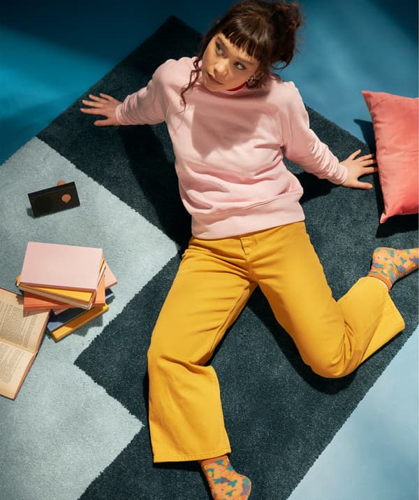 A student sitting on a rug in a relaxed manner surrounded by books and a wireless speaker.