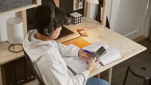 A student wearing headphones is sitting at a desk on his phone