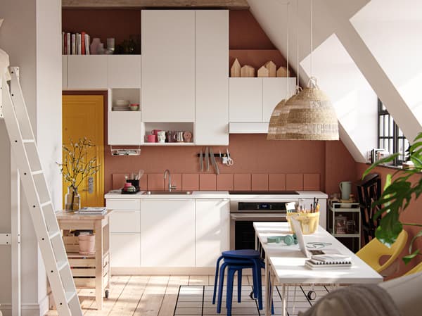 A studio apartment with large industrial-style windows, dark terracotta-coloured walls and white VALLSTENA kitchen fronts.