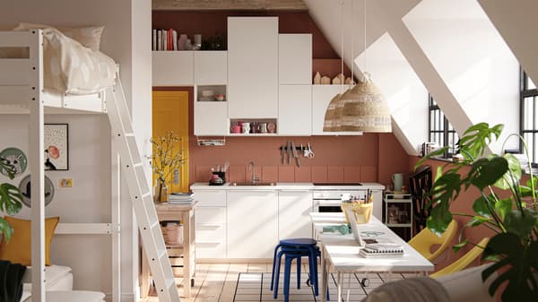 A studio apartment with large industrial-style windows, dark terracotta-coloured walls and white VALLSTENA kitchen fronts.