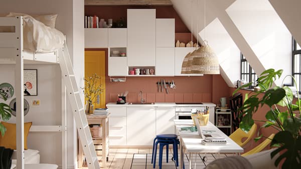 A studio apartment with large industrial-style windows, dark terracotta-coloured walls and white VALLSTENA kitchen fronts.