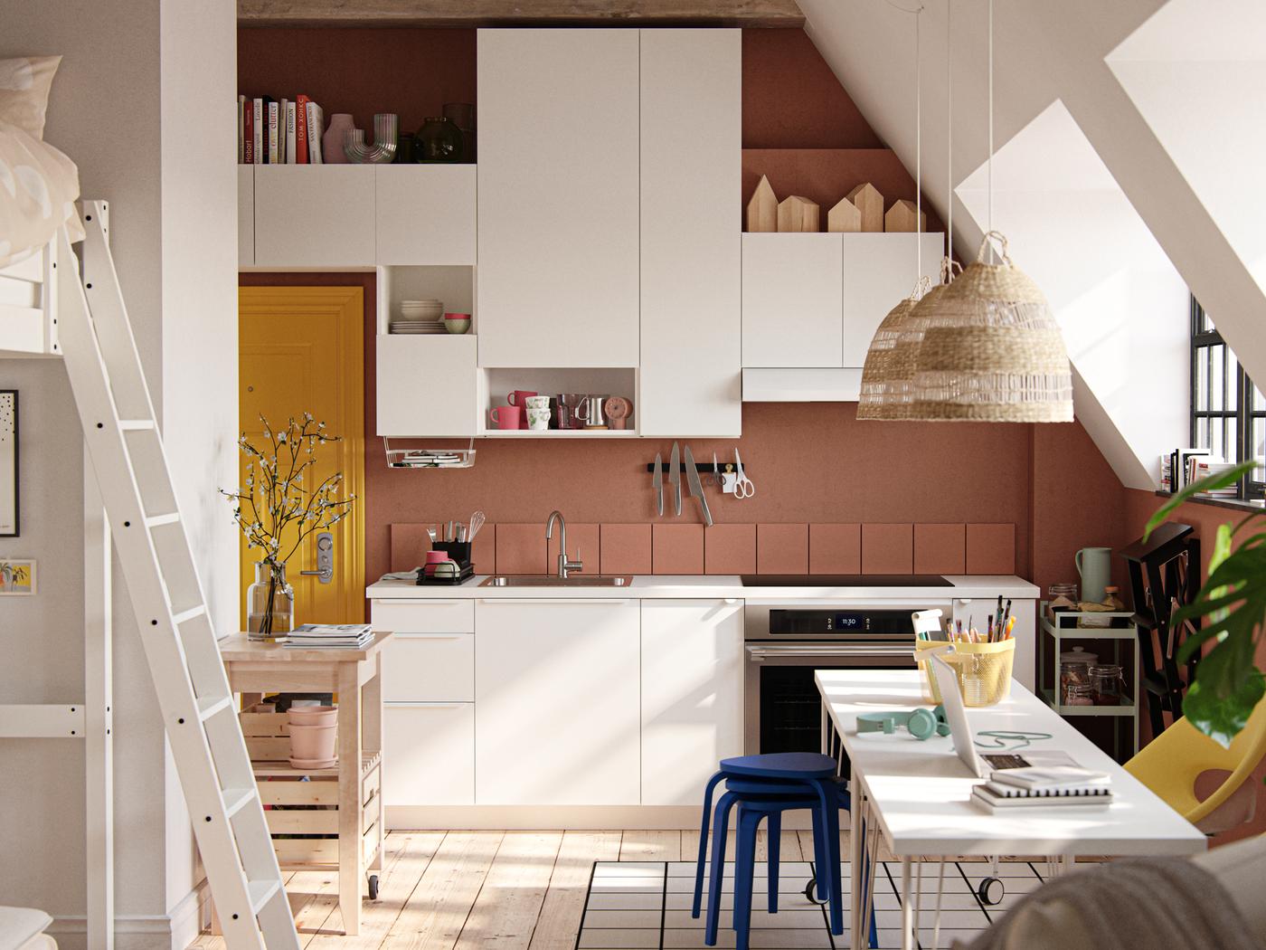 A studio with sloped ceiling, industrial-style windows, dark terracotta-coloured walls and white VALLSTENA kitchen fronts.